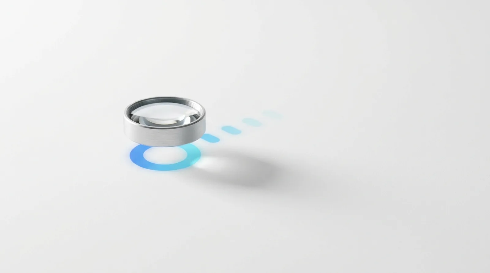 A lens in a machined ring hovering above a white surface, leaving a faint lit mark beneath it and a trail of fainter marks behind.