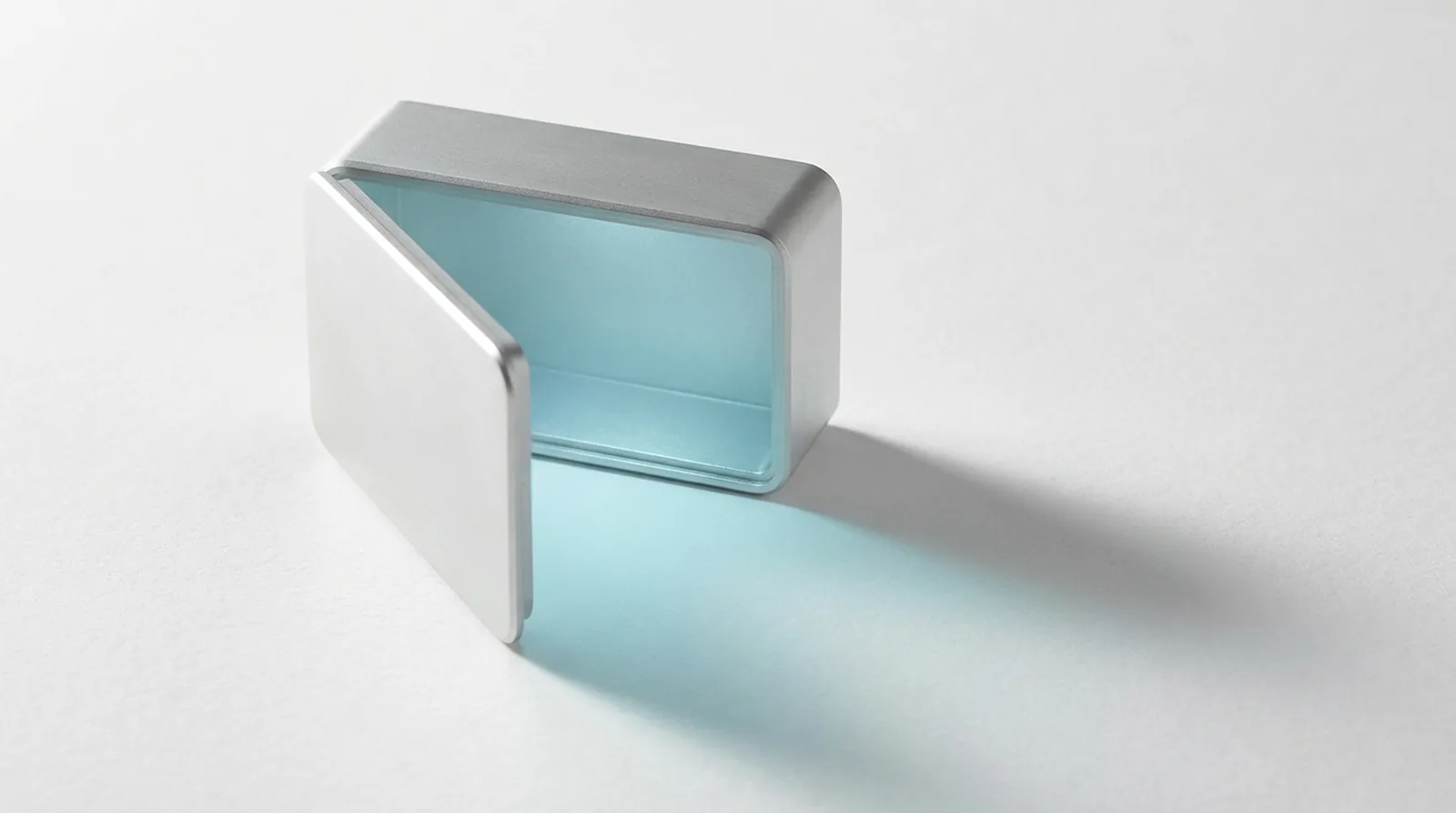 A machined enclosure standing fully open on a white ground with no lock or latch of any kind, a broad field of soft light spilling out of it.